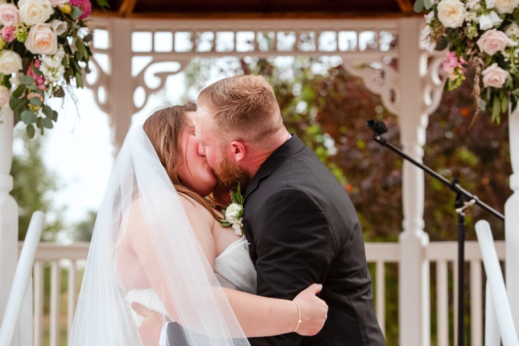 First kiss beneath the flower-decorated wedding gazebo